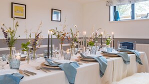 A dining table set with candles, glassware, and blue linens in a well-lit room with framed pictures on the walls.