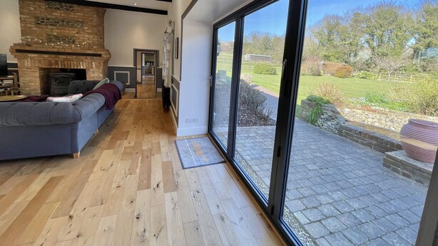 A modern living room with a fireplace, a sofa, and large sliding glass doors leading to a garden.