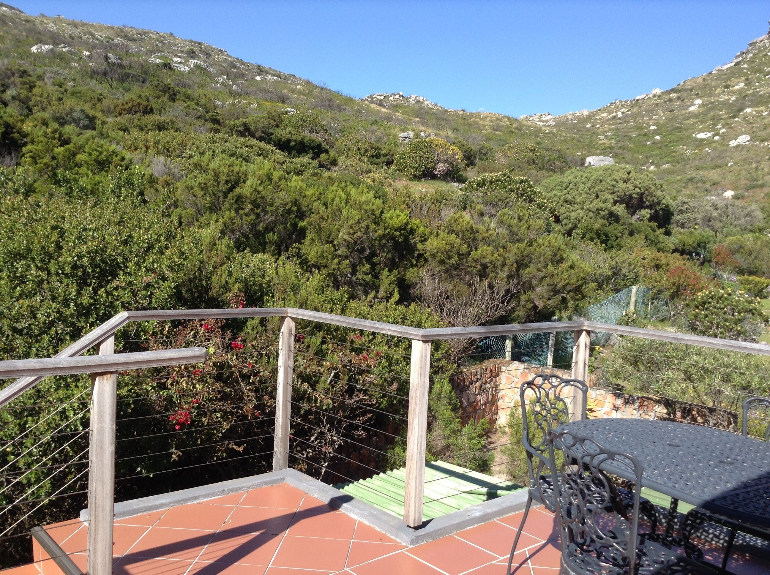 A terrace with a metal railing, terracotta tiles, and a view of a mountainous landscape with greenery.