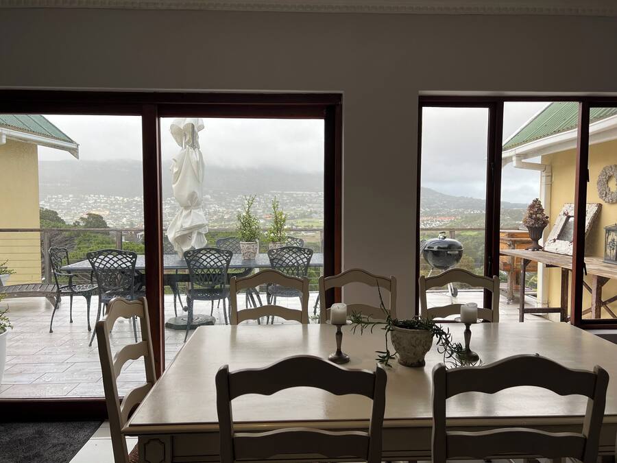 A dining area with a table and chairs, a view of a cityscape through large windows, and a statue outside.