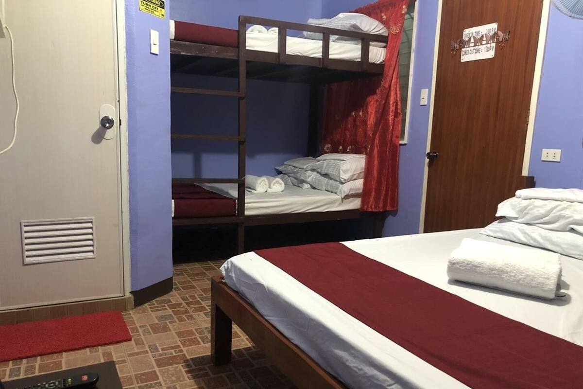 A room with a bunk bed, a single bed, a door with a sign, and a pair of remote controls on the floor.