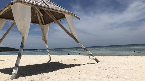 A beach hut with a thatched roof and white fabric walls, situated on a sandy beach with the ocean in the background. - Seaview Beach Resort (Anda)