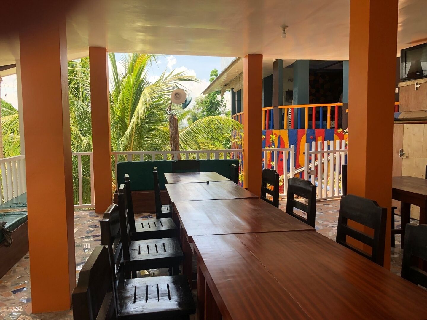 Un espace extérieur abrité, aménagé pour les repas, avec une longue table en bois et des bancs, entouré d’une clôture blanche et de jeux colorés.