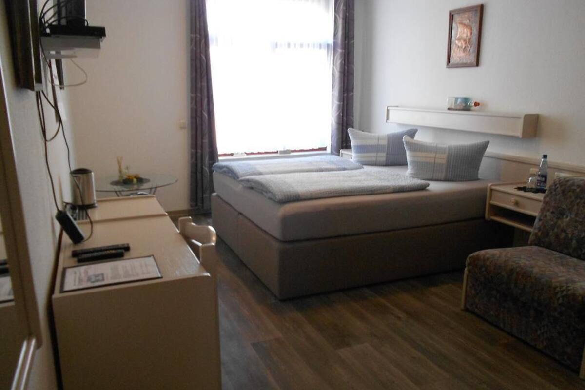 A hotel room with a bed, a desk, a chair, and a small table with a cup and a bottle.