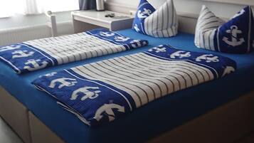 Ein Doppelbett mit bluer und weisser Streifenauflage, zwei Nachttische, ein Kopfteil und ein Fenster mit Vorhängen.
