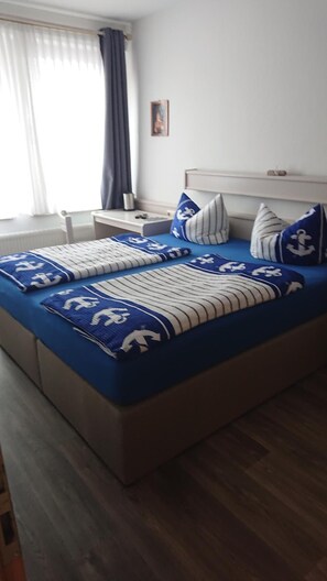 A double bed with a blue and white striped bedspread, two nightstands, a headboard, and a window with curtains. - Kajüte (Brake)