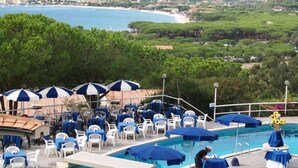 A pool area with multiple lounge chairs and umbrellas, a pool, and a view of a coastal town and hills in the background.