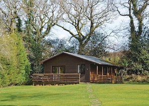 A rustic wooden cabin with a porch, surrounded by trees and a grassy field. - Ruthern Valley Holidays (Bodmin)