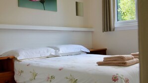 A neatly made bed with floral bedding, a bedside table, and a window with curtains.