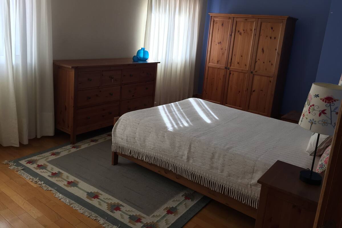 A bedroom with a bed, wooden dresser, wardrobe, and a lamp.