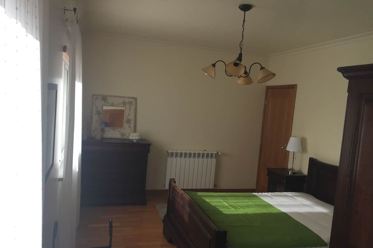 A bedroom with a bed, a dresser, a radiator, and a ceiling light fixture.