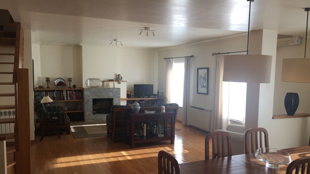 A spacious living room with a fireplace, wooden flooring, a dining area with a table and chairs, and a television. - Apartamento Senadomum (Seia)