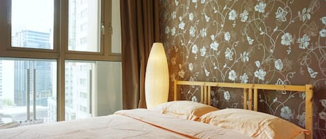 A hotel room with a large bed, floral wallpaper, and a view of buildings through a window.
