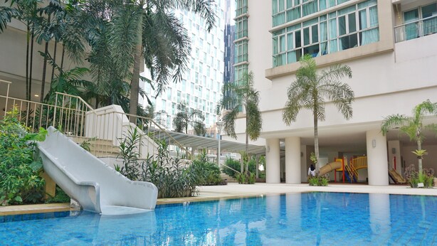 Una piscina interior con tobogán, rodeada de palmeras y un edificio de varios pisos con grandes ventanales.