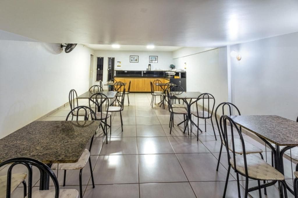 A dining area with tables and chairs, a kitchen in the background, and a tiled floor.