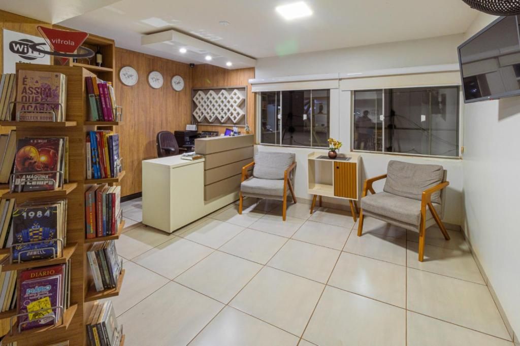 A modern living room with a desk, two chairs, a bookshelf, and a large window.