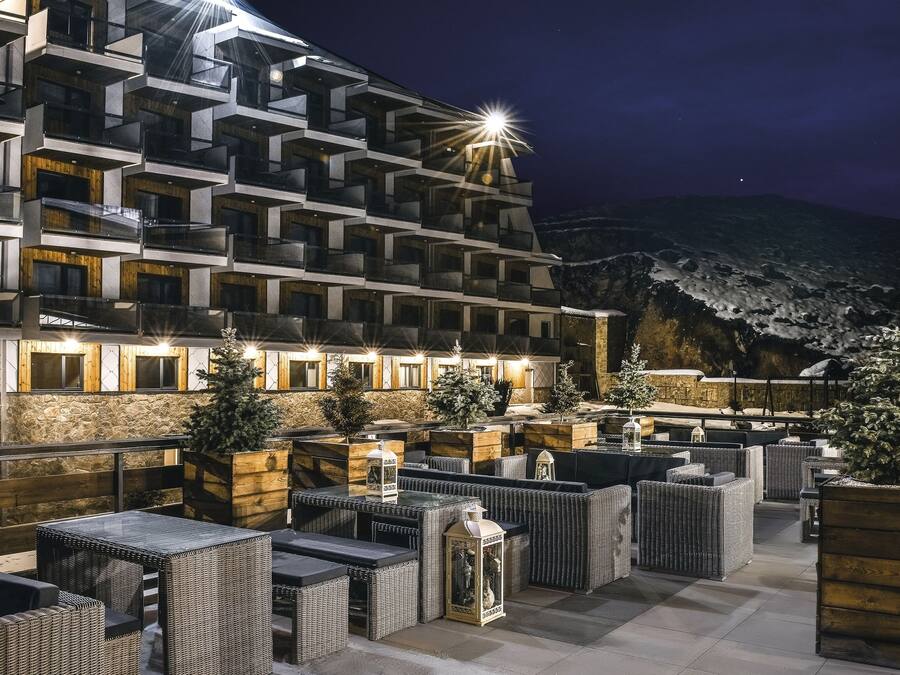 A modern hotel with multiple balconies, outdoor seating areas, and a view of a mountainous landscape.