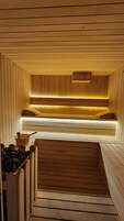 A sauna with wooden walls and benches, a sloped ceiling, and a wooden bench with a bench runner.