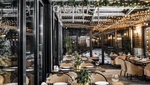 Un área de comedor al aire libre con sillas y mesas de mimbre, luces colgantes y vista a la calle.