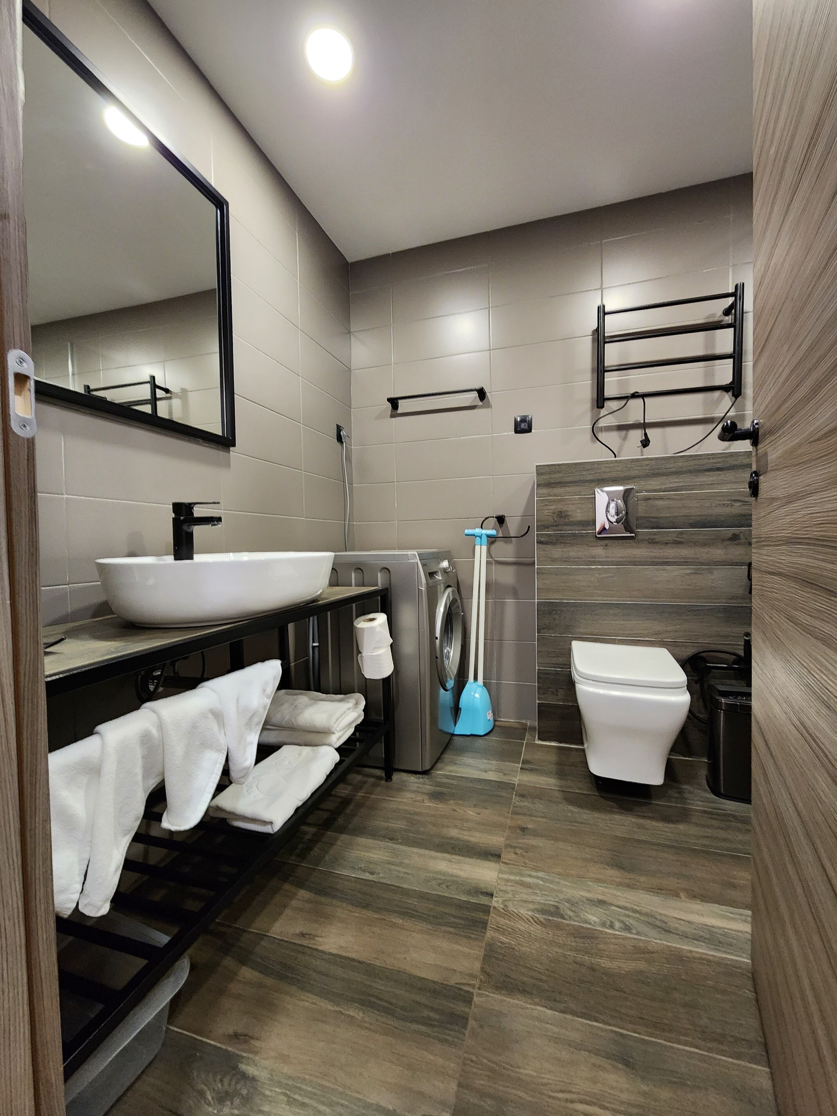 A modern bathroom with a large sink, a toilet, a washing machine, and a mirror.