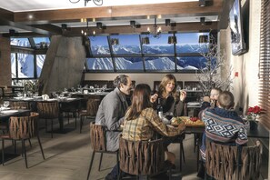 A restaurant with multiple tables and chairs, large windows with mountain views, and a modern interior design. - Gudauri Hills ApartHotel (Kazbegi)