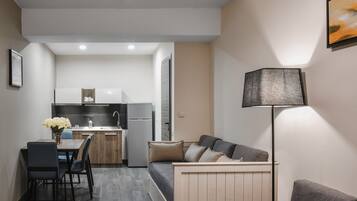 A compact living space with a kitchenette, a dining area, and a seating area with a sofa and a lamp.