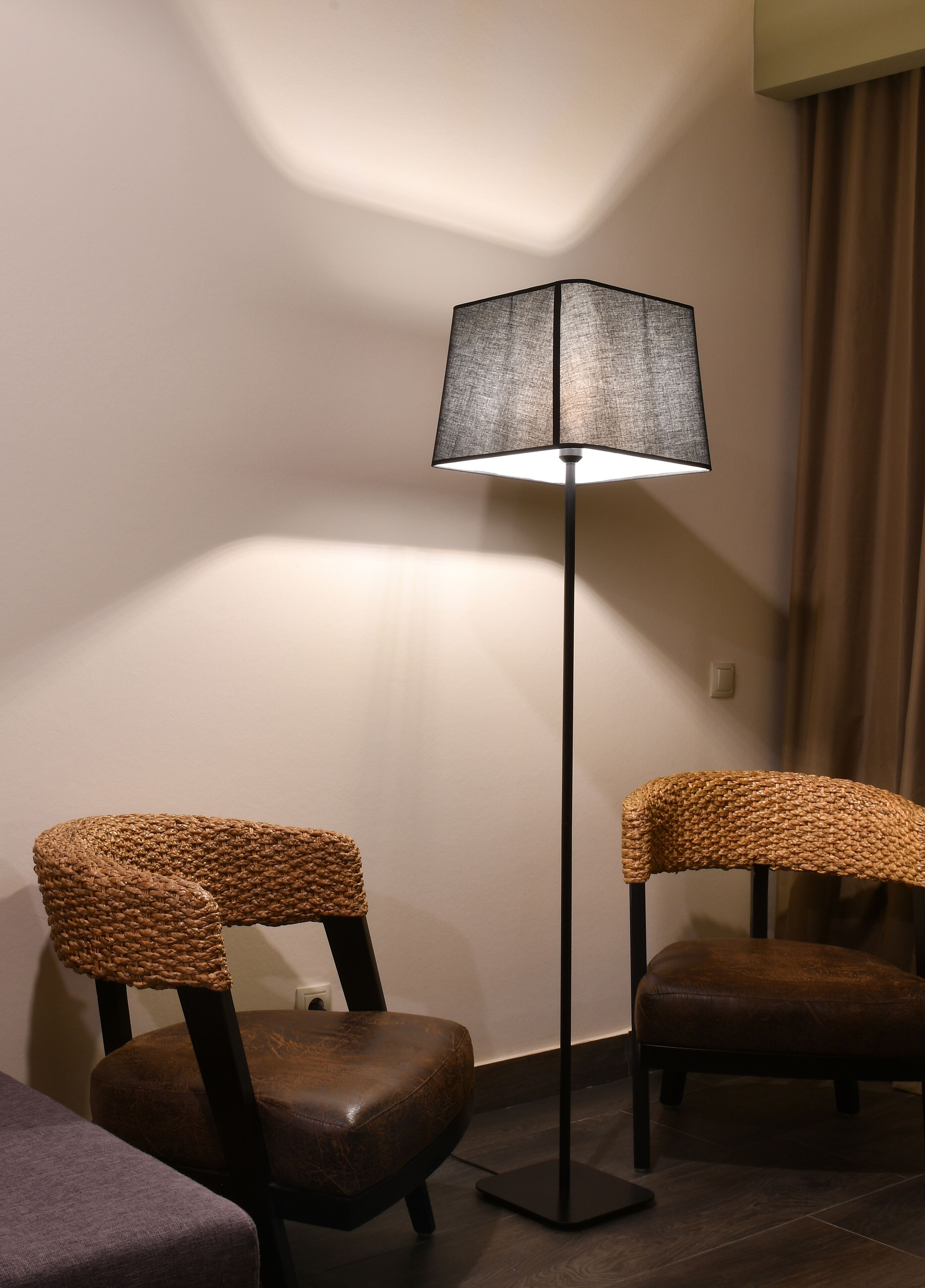 A modern room with a floor lamp, two wicker chairs, and a dark wooden floor.