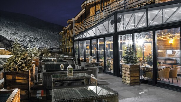 Un restaurante con terraza, grandes ventanales y vistas a una montaña nevada.