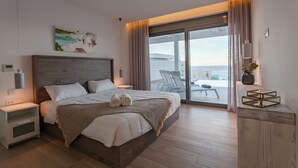 A modern bedroom with a large bed, a nightstand, a bedside table, a window with curtains, and a view of the sea. - Villa Faros (Rhodes)