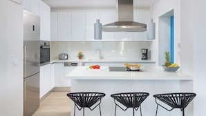 A modern kitchen with white cabinetry, stainless steel appliances, a central island with seating, and a blue accent wall. - Villa Faros (Rhodes)