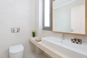 A modern bathroom with a white toilet, a beige sink, and a large mirror above the sink.