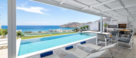 A modern outdoor pool area with lounge chairs and a view of the ocean.