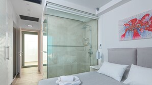 A modern hotel room with a large bed, a glass shower enclosure, and a view of the outside. - Villa Vrachos (Rhodes)