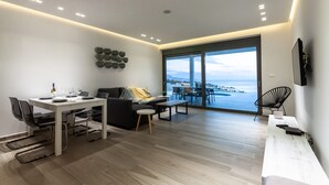 A modern living room with a dining area, a sofa, a coffee table, and a view of the sea. - Villa Vrachos (Rhodes)