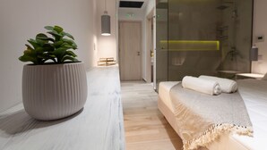 A modern hotel room with a large potted plant, a neatly made bed with a towel, and a glass shower area. - Villa Vrachos (Rhodes)