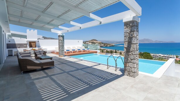 Un espace de détente extérieur moderne, doté d’une piscine, de piliers en pierre et offrant une vue sur la mer.
