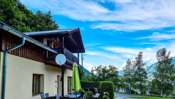 A wooden building with a balcony, outdoor seating, and a view of a mountainous landscape. - Lake View Lodges - Penthouse (Zell am See)