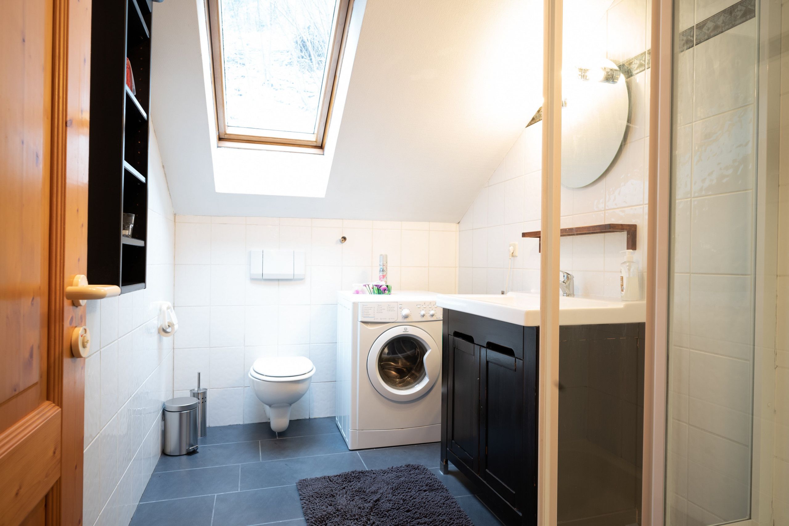 A compact laundry room with a washing machine, a toilet, and a skylight.