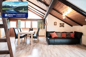 Une pièce chaleureuse avec un plafond en bois, un canapé en cuir noir, une table à manger avec des chaises, et une vue sur les montagnes par la fenêtre.