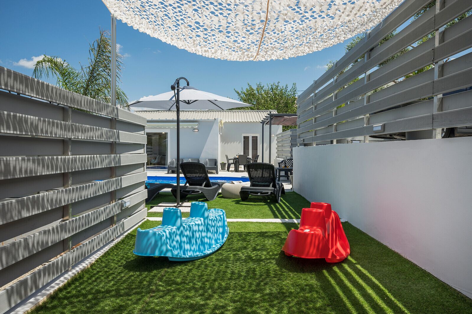 A modern outdoor patio with artificial grass, a pool, and outdoor furniture.