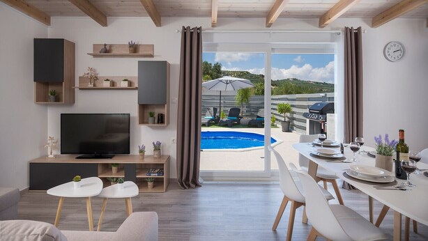 A modern living room with a TV, seating, and a dining area with a pool view. - B&M Villa Sirili (Platanias)