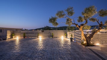 A paved outdoor area with a wooden fence, potted plants, and a tree.