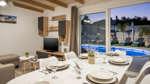 A modern living room with a dining area set for a meal, a TV, and a view of a swimming pool. - B&M Villa Sirili (Platanias)