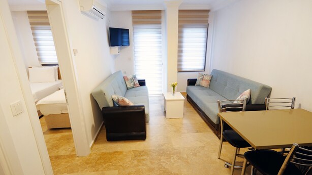 Un espace de vie compact comprenant un canapé, un pouf, une petite table et un téléviseur fixé au mur.