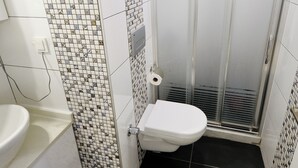 Une salle de bain avec un mur carrelé, des toilettes, un lavabo et un espace douche.