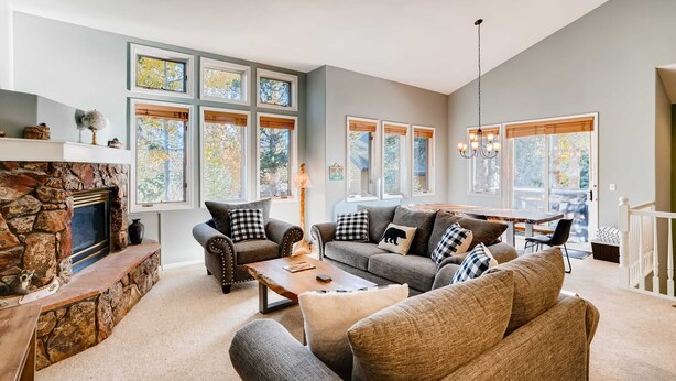 A spacious living room with a stone fireplace, multiple windows, and a staircase.