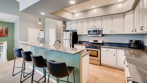 A modern kitchen with white cabinets, a central island with bar stools, stainless steel appliances, and recessed ceiling lighting.
