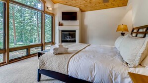 Ein Schlafzimmer mit großem Fenster, Kamin, Bett und Fernseher.