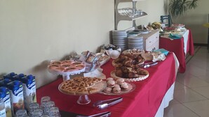 Una mesa de buffet con diversos alimentos y bebidas, incluyendo una variedad de pasteles, sándwiches y una tarta.