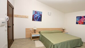 Un dormitorio con una cama, mesitas de noche, un armario y dos cuadros en la pared.
